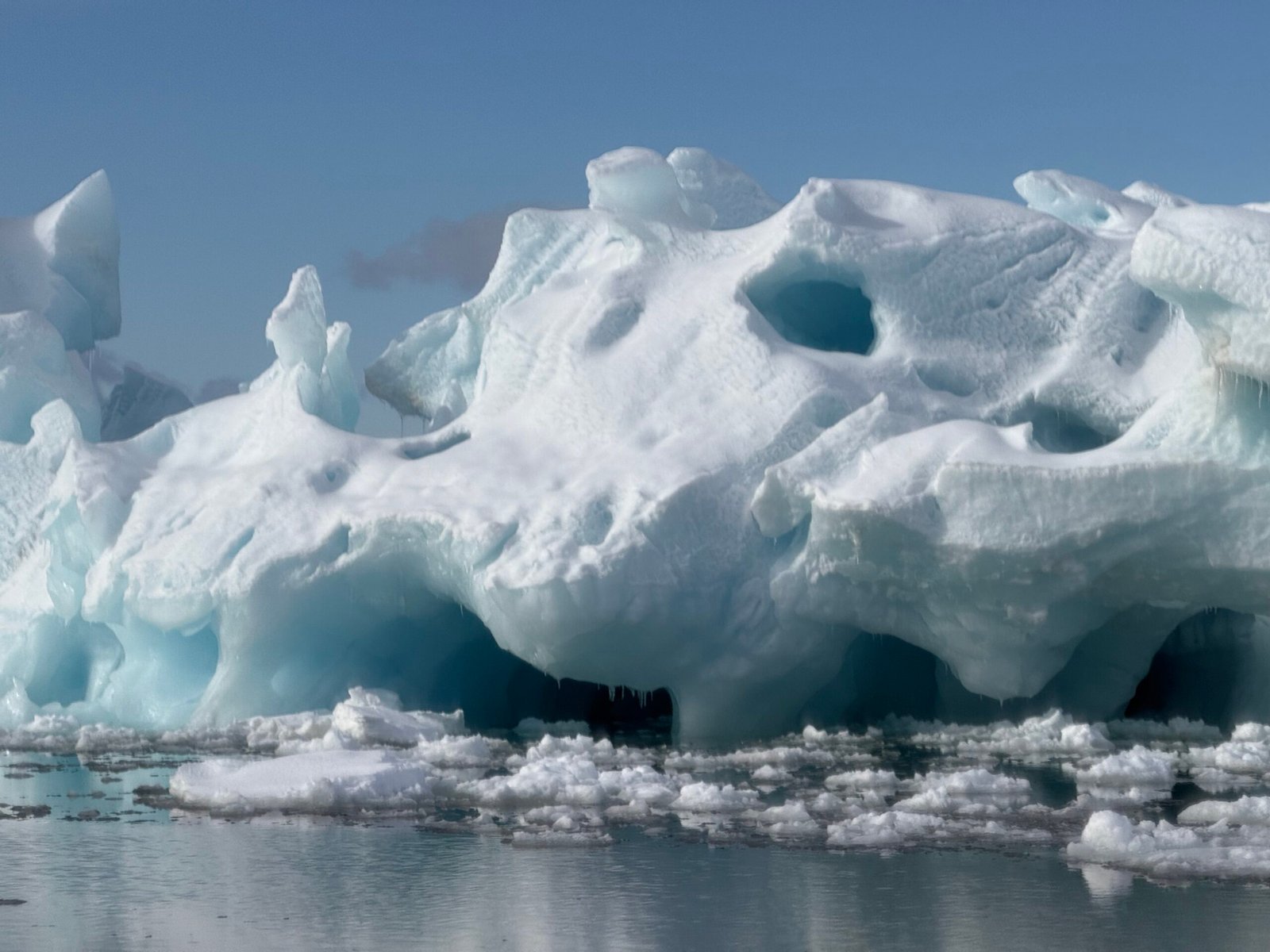 Wind-sculpted blue-white sea ice with deep openings above calm arctic water.