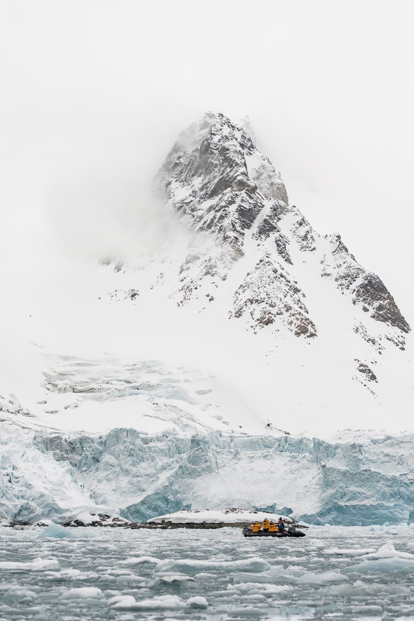 Expedition Zodiac cruising through icy water beneath a snow-covered Svalbard mountain