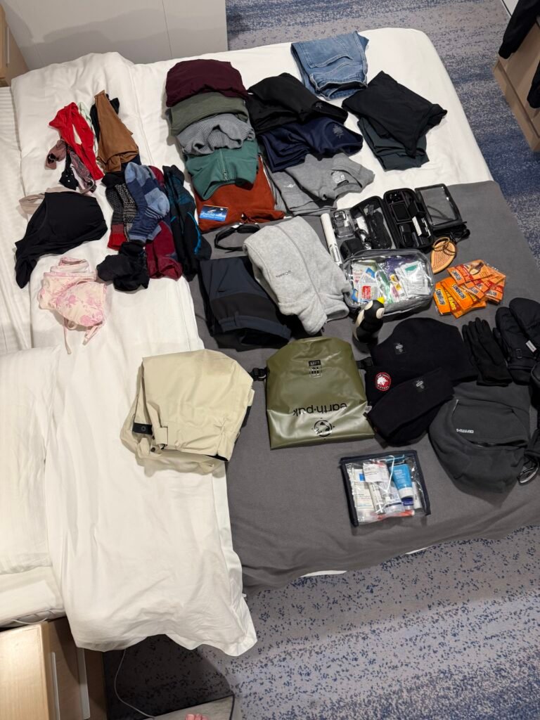 Polar expedition packing list laid out on a bed: wool base layers, fleece, Gore-Tex over pants, dry bag, hats, gloves and toiletries.