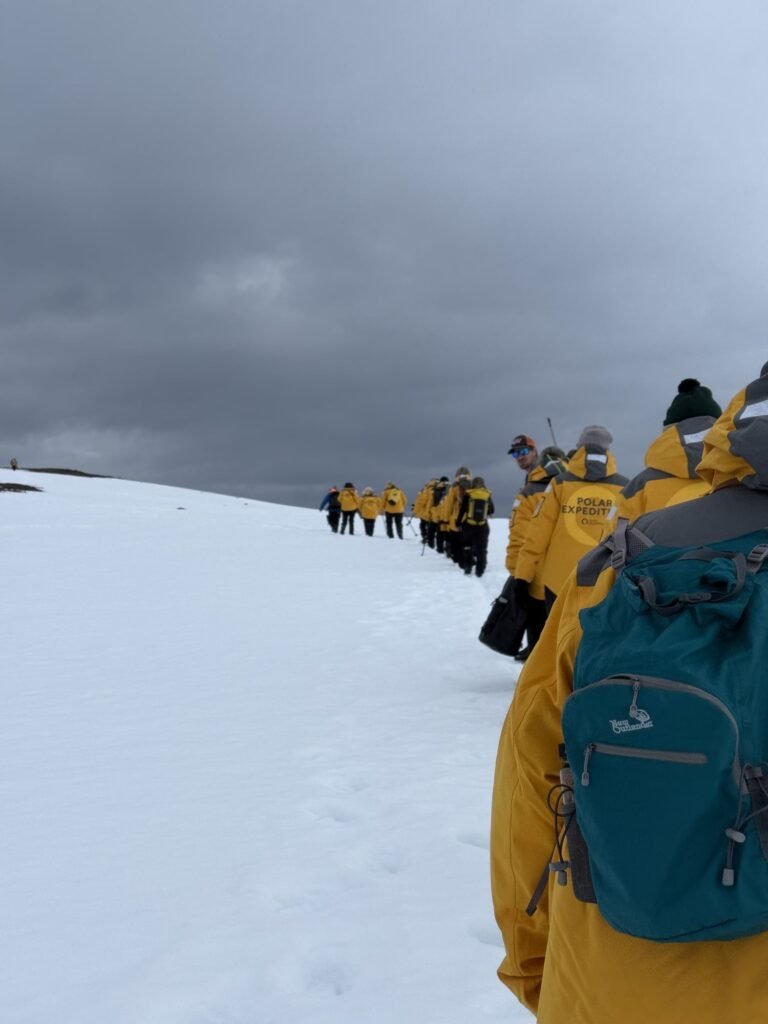 Expedition guests in yellow parkas following their guides across the snow in Svalbard