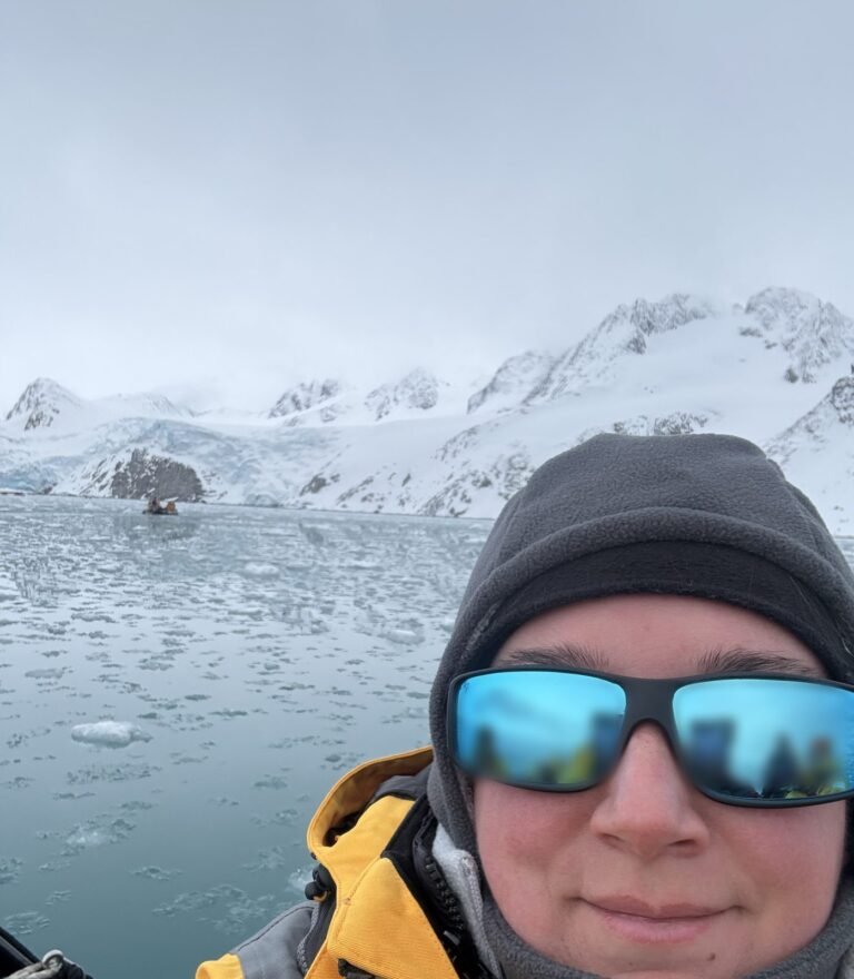 Amanda smiling in a yellow expedition parka and sunglasses on a Zodiac cruise in Svalbard